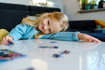 Caucasian blonde cute happy girl 4 years old playing puzzles at home. Toddler kid connecting jigsaw...