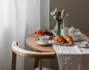 Cozy breakfast - a set table with tea cups, a plate of fruits and berries, croissants