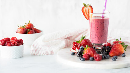 A very berry smoothie surrounded by berries and garnished with a strawberry.