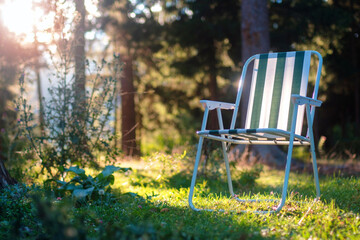 Empty folding camp chair for relaxing on the field near the forest with blurred sunset background