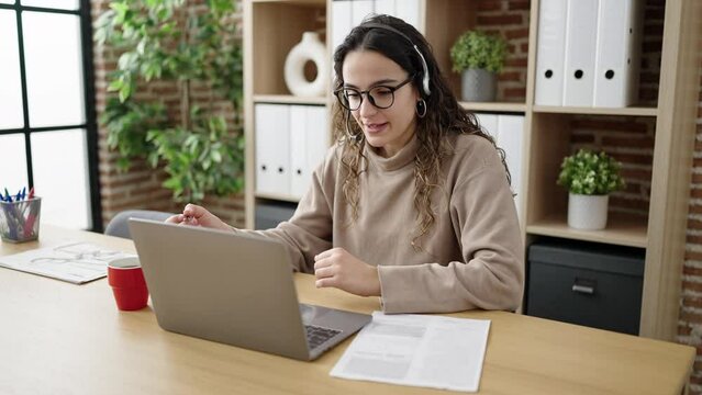 Young beautiful hispanic woman business worker having video call writing document at office