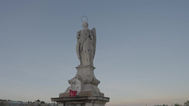 Statue of the Archangel Raphael stands in the middle the ancient Roman bridge, looking out across the river towards the old city of Cordoba, Spain