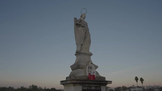 Statue of the Archangel Raphael stands in the middle the ancient Roman bridge, looking out across the river towards the old city of Cordoba, Spain