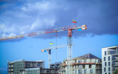 Construction site with cranes with flags Lithuanian and Ukrainian building residential buildings on blue sky background with fluffy dark clouds