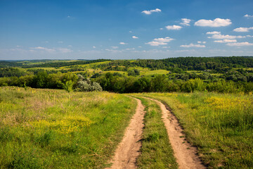 Fototapeta na wymiar summer country road amidst green hills and blue sky with white clouds