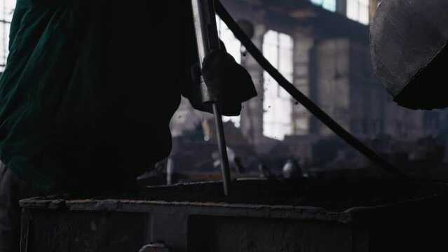 Steel making process of man tapping sand into the casts. Workers in factory using construction tools while working.