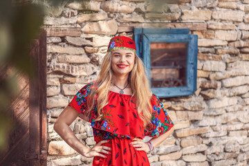 Portrait of beautiful gypsy woman in traditional red dress standing in front of romani camp - obrazy, fototapety, plakaty