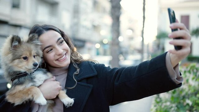 Young hispanic woman with dog smiling confident make selfie by smartphone at street