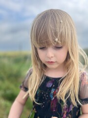 little blonde girl with flowers in her hair stands against the sky. Soft focus. 