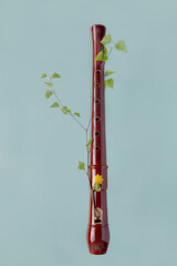 wooden block flute wrapped with a branch with leaves on a blue background