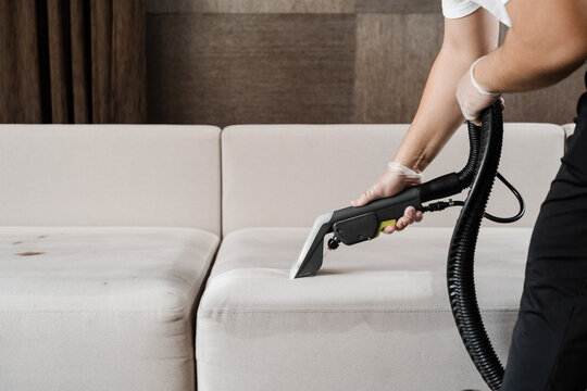 Housekeeper is extracting dirt from upholstered sofa using dry cleaning extractor machine. Cleaning couch with washing vacuum cleaner extraction machine for dry clean upholstered furniture.