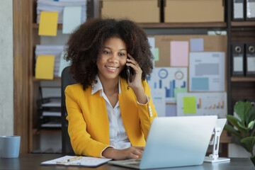 Obraz premium African American businesswoman working on mobile phone with laptop computer and finance marketing chart, Advisor showing plan of investment to clients at office desk. Digital marketing online concept.