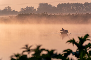 a fisherman casting nets on a boat into the river at dawn.