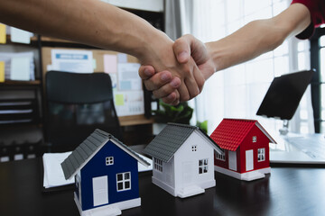 Business man and woman in formal attire shaking hands, and sell home model.  