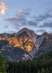 Stunning mountain view. Picturesque landscape with beautiful sharp rocks. Part of the rock is illuminated by the sun's rays of light. Beautiful mountain landscape. At the foot of a dense green forest