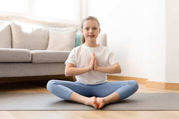 Fototapeta na wymiar Smiling caucasian middle aged girl in sportswear practicing yoga, meditates on mat in living room