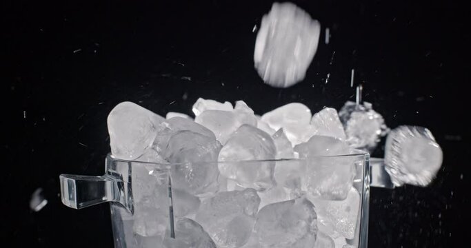 Ice cubes from an ice maker are put into a glass container with ice. Slow motion video