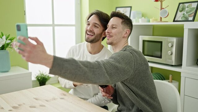 Two men couple taking selfie picture by smartphone drinking glass of wine at dinning room