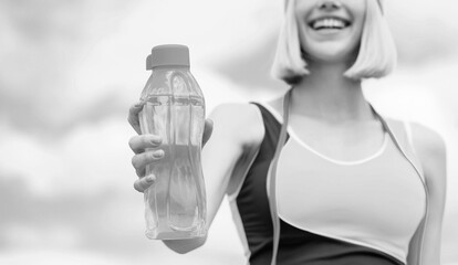 Woman drinking water after run. Sports girl drinks water from a bottle on a sky background. Drinking during sport. Black and white