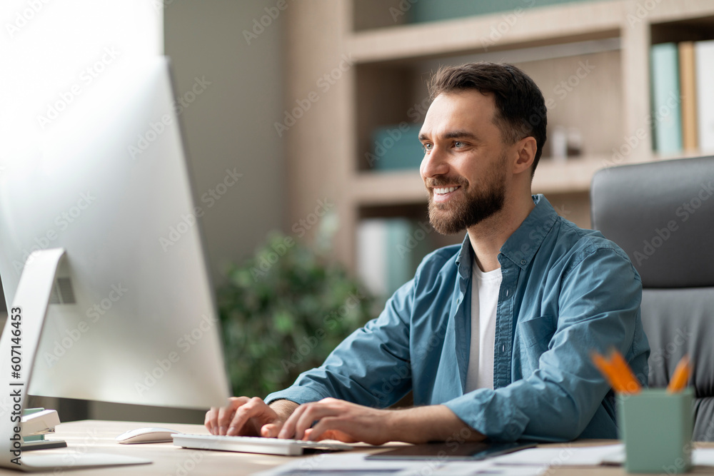 Poster portrait of smiling millennial businessman working on computer in office