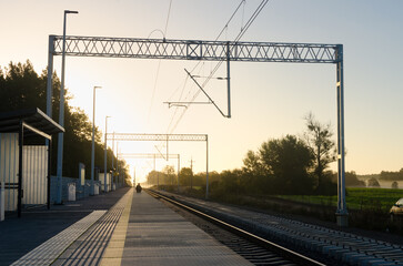 Fototapeta na wymiar Serenity at Sunset: Railway Landscape with Train Tracks Leading into the Distance, Station Stop, Fields, and a Person Waiting for the Train