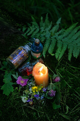 Burning candle, magic potion bottles, flowers on dark forest natural background. Magic ritual,...