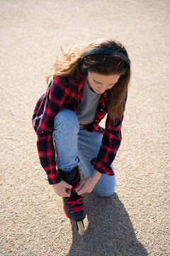 Young pretty woman with headphones tying her skate laces. Woman listening to music and roller skating