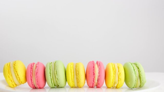 the sleeve of a yellow glove is ironing showing a selection of different colors of macaroons green yellow pink on a white background Macaroons or macaron on pastel blue surface. Close up.