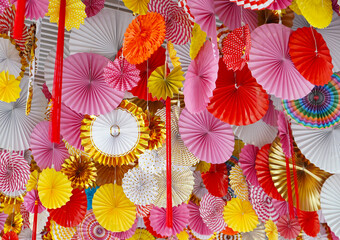 Fototapeta na wymiar Festive paper fans of different colors red, lilac, yellow, white hang as a holiday decoration