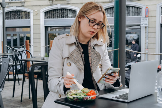 Woman Eats A Healthy Lunch Salad With Avocado Chicken Tofu And Tomato And Looks At Her Smartphone