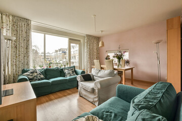 a living room with green couches and floral curtains on the windows looking out onto an outside patio area that has wooden flooring