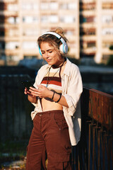 Beautiful young blonde listens to music through headphones and a smartphone in the city