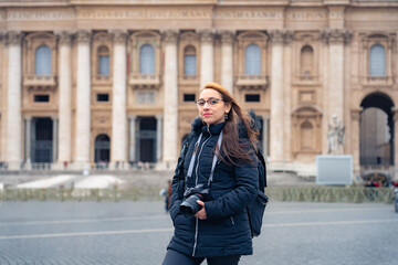 Fototapeta premium Full body of young Latin woman tourist in trendy clothes with professional photo camera standing in front of historic church Saint Peter Basilica in Vatican city, Rome, Itay