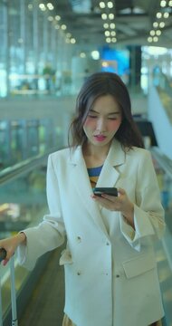 Business woman using phone at escalator in airport. Asia woman commuter travels with luggage on escalator.