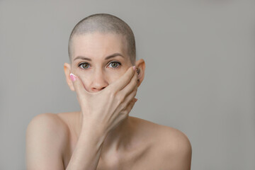 Portrait of an emotional young beautiful woman with a shaved head close-up, she covers her mouth with her hand. The result of chemotherapy in the treatment of breast cancer