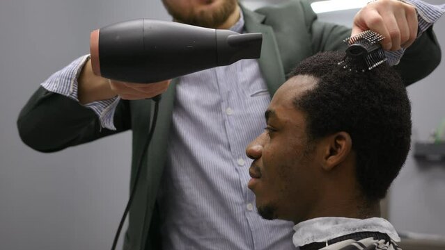 Barber drying afroamerican man's hairs grooming styling haircut use hair dryer.