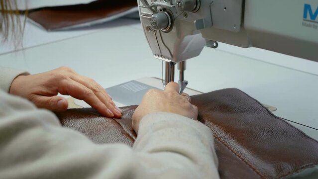 Close-up view of working sewing machine stitching leather. Tailor's hands holding sewing leather carefully. Manufacturing handicraft accessories for furniture.