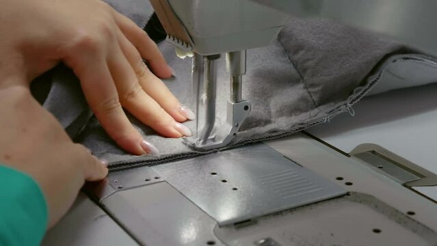 Close-up view of woman hands working sewing machine stitching fabric. Professional seamstress workshop busy day.