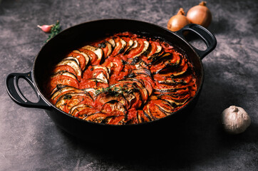French ratatouille with tomatoes, eggplant, zucchini and fresh herbs in a cast iron skillet against...