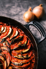 French ratatouille with tomatoes, eggplant, zucchini and fresh herbs in a cast iron skillet against...