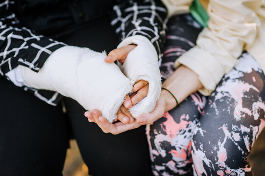 A caring woman, mother, girlfriend holds hands in a cast, bandage an injured sick girl, a child after a bone fracture, cares, calms, helps. Close-up photography, portrait, rehabilitation.