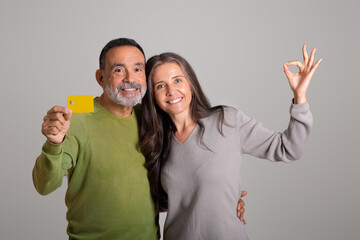 Positive european old couple with credit card enjoy online shopping remotely, show ok hand sign