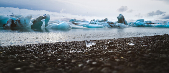 Jökulsarlon lagoon in south-east iceland - little pieces of ice on the black gravel beach in front of large ice bergs floating in the lagoon, banner, header © Sonja Birkelbach