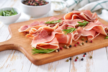 traditional prosciutto di parma with fresh rosemary on a wooden table.