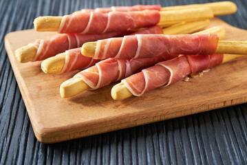 Parma ham prosciutto with Italian grissini breadsticks on a black wooden table .