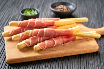Parma ham prosciutto with Italian grissini breadsticks on a black wooden table .