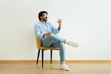 Cheerful millennial middle eastern guy blogger in glasses has video call, shooting blog on...