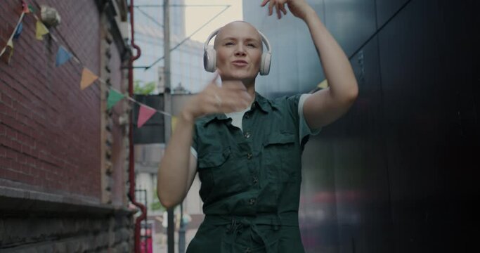 Slow motion portrait of joyful lady wearing headphones dancing to music in modern city alone. Youth lifestyle and contemporary dance concept.