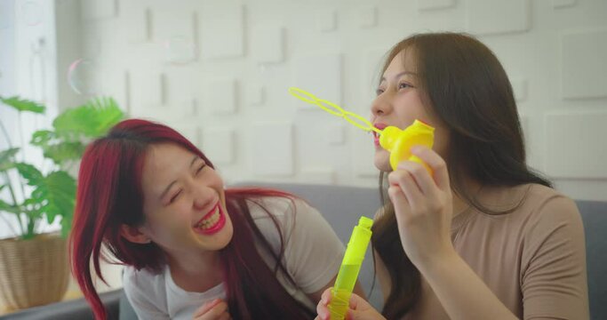 Asian young women playing pub together at home. She blows bubbles in a funny way.