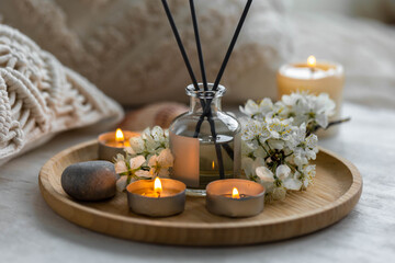 Aroma diffuser, burning candle, cherry blooming flowers and perfume on wooden bamboo tray. Cozy...